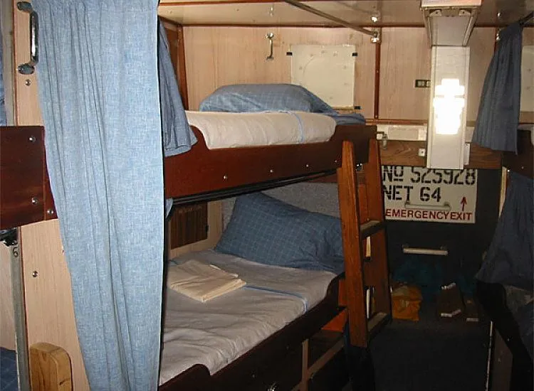 Slide: The Image of 1970 Custom Dive Vessel bunk beds cabin interior with blue curtains and bedding. - 12
