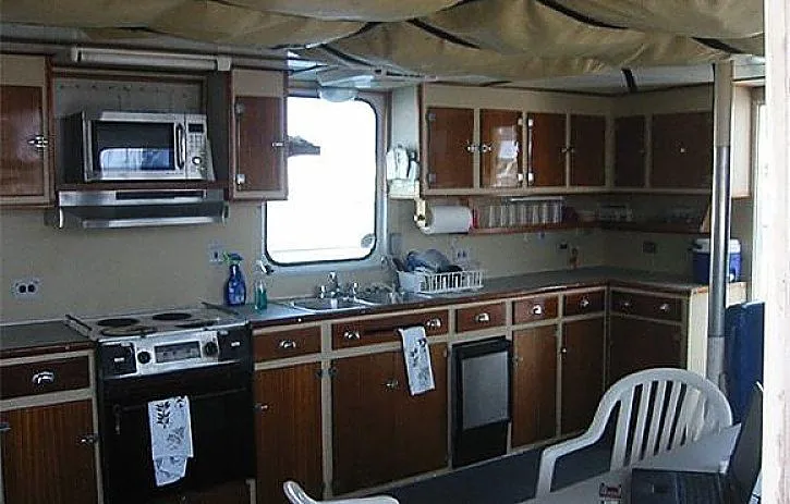 Slide: The Image of 1970 Custom Dive Vessel kitchen with wooden cabinets, stove, microwave, and sink. - 13