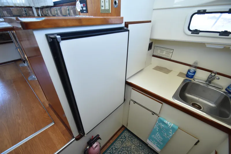 Slide: The Image of Compact kitchen area in a 2001 Camano 31 Trawler with sink, fridge, and wooden accents. - 33