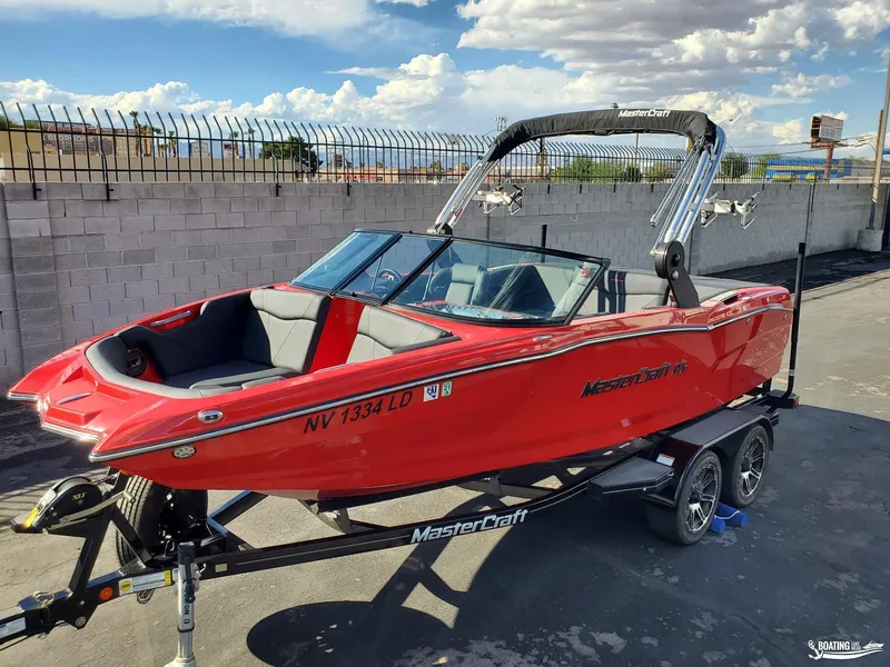 Slide: The Image of 2020 MasterCraft NXT20 red boat on trailer, parked outdoors under cloudy sky. - 2