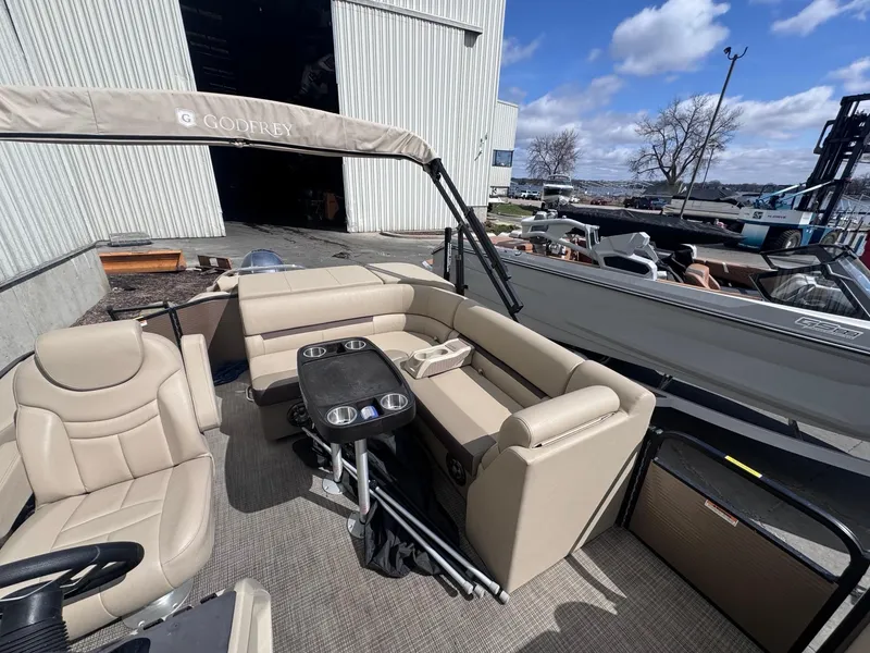 Slide: The Image of 2022 Sweetwater SW 2286 C pontoon boat with beige seating and table, docked near a warehouse. - 8