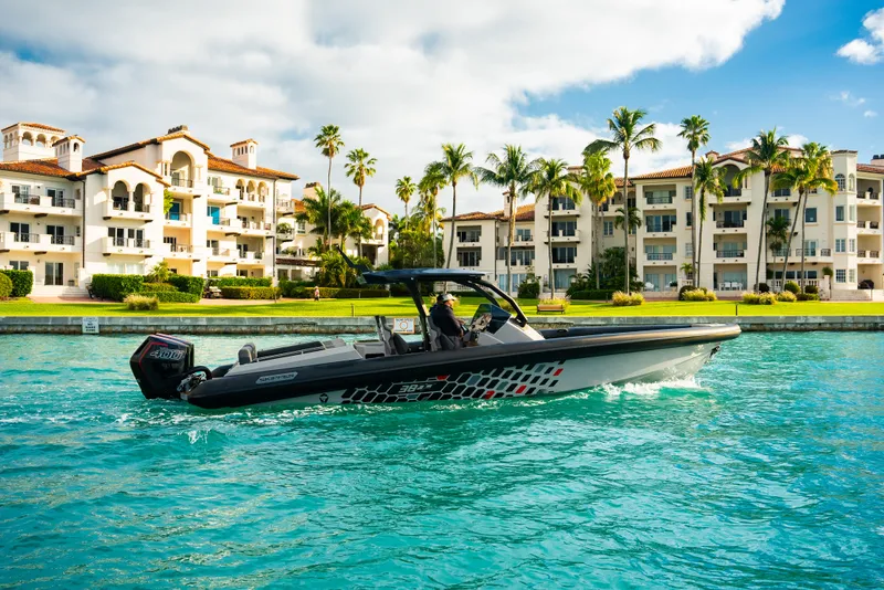Slide: The Image of 2024 Skipper-BSK 38NC boat cruising near luxury waterfront apartments. - 1