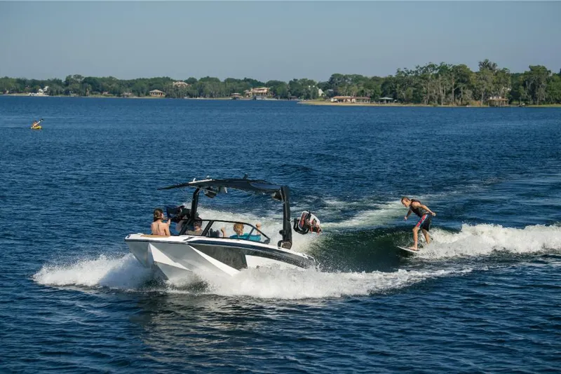 Slide: The Image of 2023 Nautique Super Air GS22E towing wakeboarders on a sunny lake. - 22