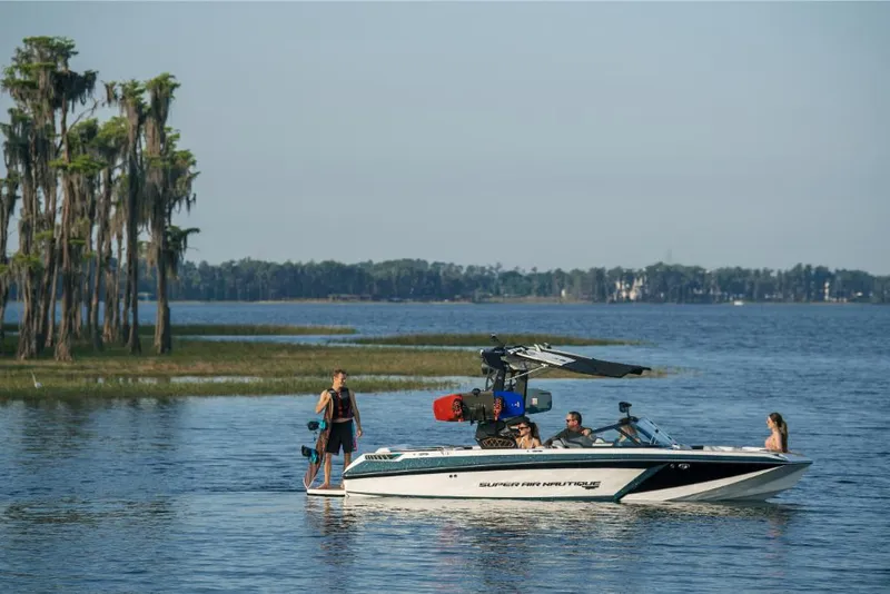 Slide: The Image of 2023 Nautique Super Air GS22E boat on a lake with people preparing for water sports. - 24
