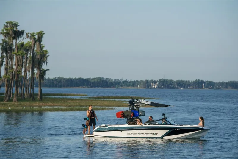 Slide: The Image of 2023 Nautique Super Air GS22E boat on a lake with people enjoying water activities. - 25
