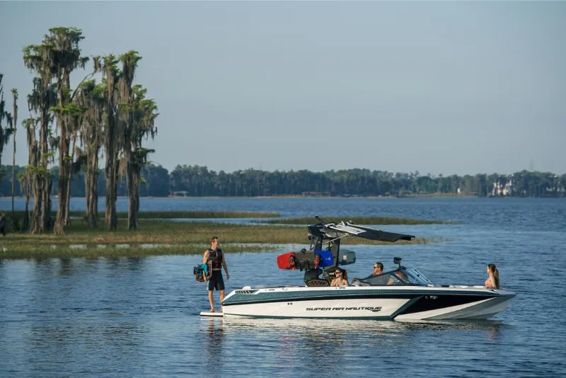 Slide: The Image of 2023 Nautique Super Air GS22E boat on a lake with people enjoying water activities. - 26
