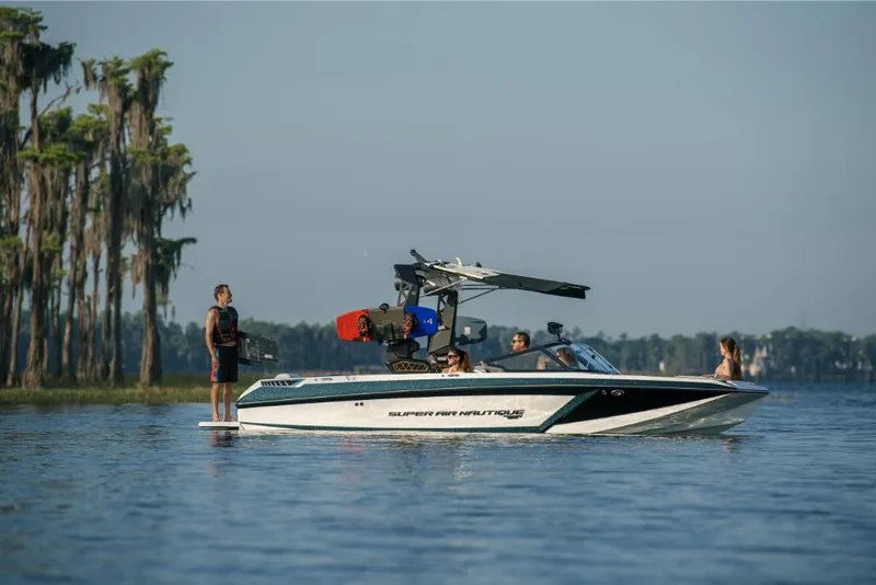 Slide: The Image of 2023 Nautique Super Air GS22E boat on a lake with people enjoying water activities. - 27