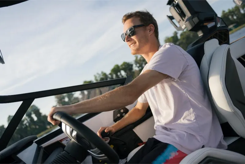 Slide: The Image of Man driving 2023 Nautique Super Air GS22E boat, enjoying sunny day on the water. - 48