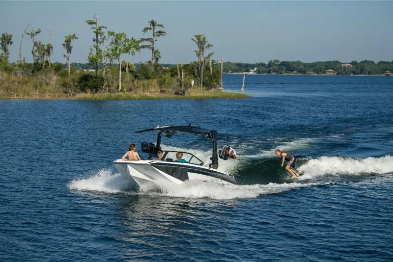 Slide: The Image of 2023 Nautique Super Air GS22E towing wakeboarders on a scenic lake. - 6