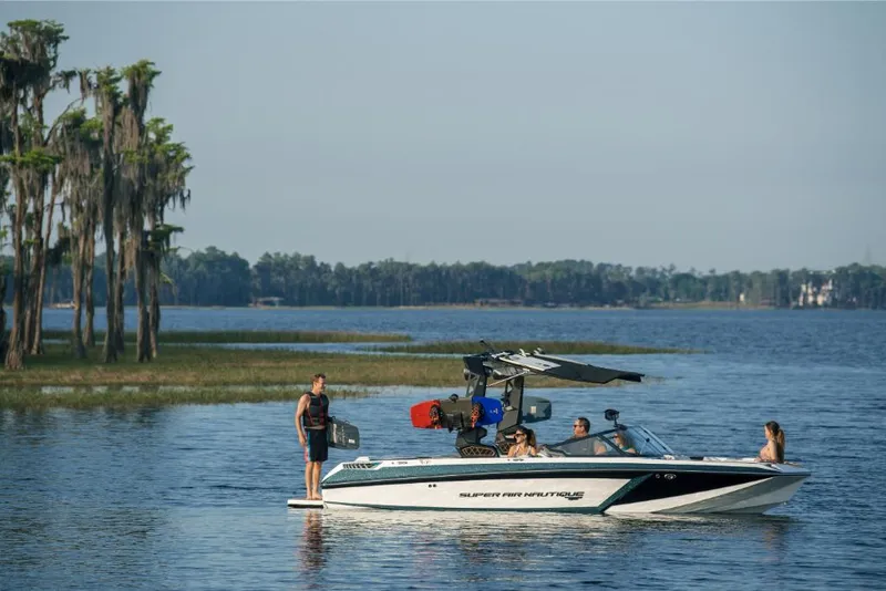 Slide: The Image of 2023 Nautique Super Air GS22E boat on a serene lake with people enjoying water activities. - 7