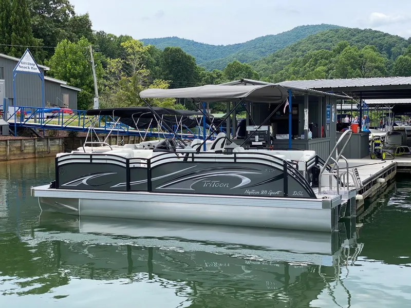Slide: The Image of 2024 JC Neptoon Sport 23TT DSL pontoon boat docked at a marina with scenic mountain backdrop. - 3