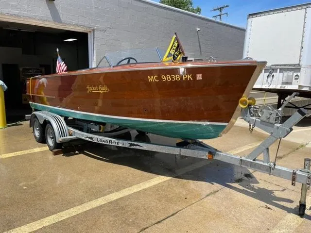 The Image of 1949 Hacker-Craft Utility boat on trailer, wooden finish, parked outside a garage. - 1