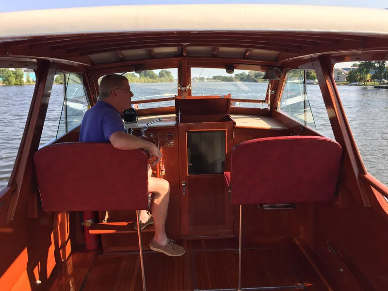 Slide: The Image of 1954 Chris-Craft Commander boat interior with person seated, navigating a scenic waterway. - 24