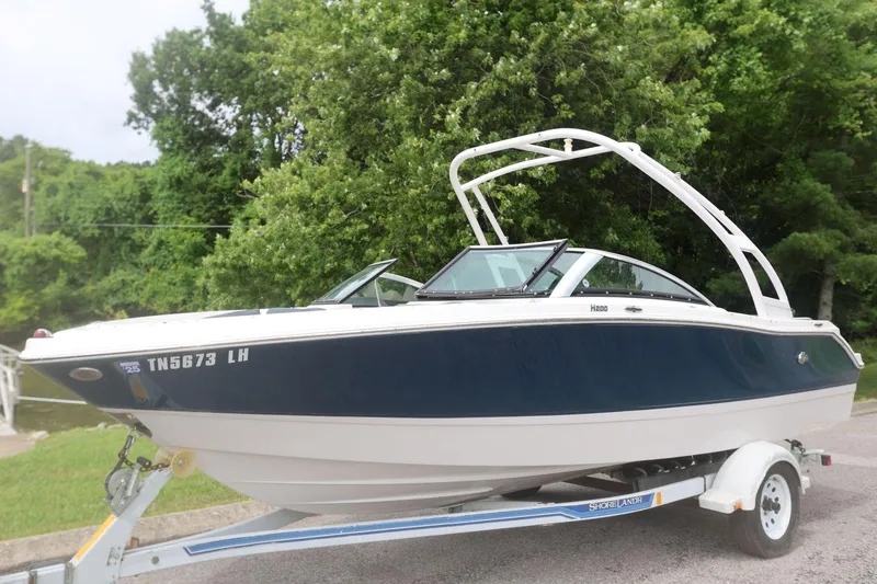 Slide: The Image of 2015 Four Winns H200 boat on trailer, parked near lush green trees. - 2
