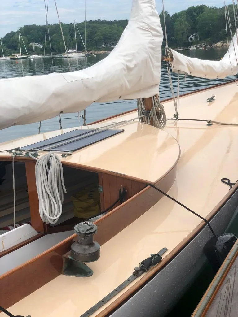Slide: The Image of 1914 Buzzards Bay 25 sailboat with white sails docked on a calm lake. - 18