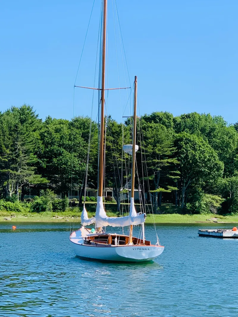 Slide: The Image of Vintage 1914 Buzzards Bay 25 sailboat on a serene lake with lush green trees. - 2