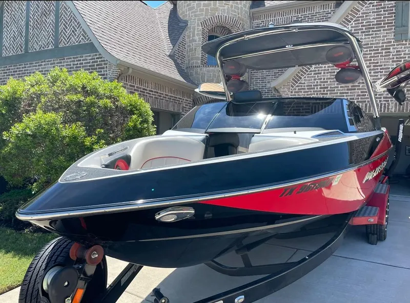 Slide: The Image of 2013 Malibu 247LSV boat with black and red exterior parked in front of a house. - 5