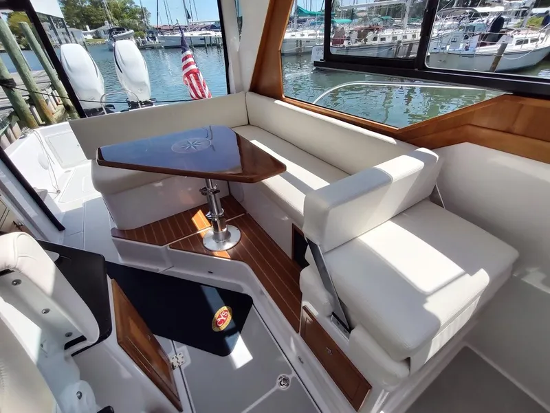 Slide: The Image of 2023 True North 34 OE boat interior with white seating and wooden table, docked at marina. - 14