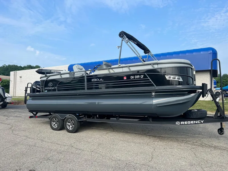 Slide: The Image of 2021 Regency 230 LE3 pontoon boat on trailer, parked outdoors. - 0