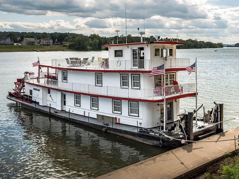 The Image of 1936 Custom Dravo Sternwheeler docked by a river with American flags. - 0