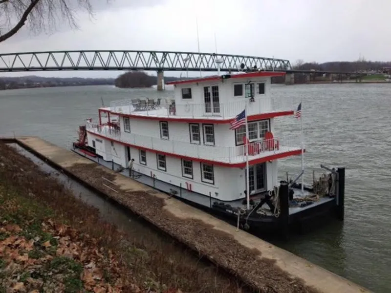 Slide: The Image of 1936 Custom Dravo Sternwheeler docked by a river with a bridge in the background. - 2