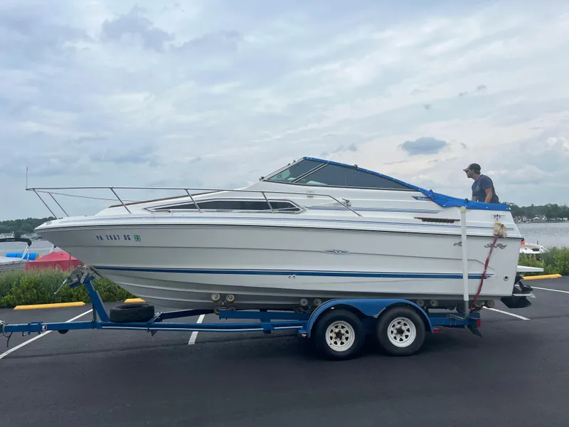 Slide: The Image of 1989 Sea Ray 230 Weekender boat on a trailer in a parking lot. - 0