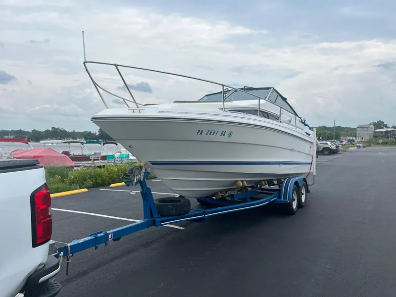Slide: The Image of 1989 Sea Ray 230 Weekender boat on a trailer in a parking lot. - 1