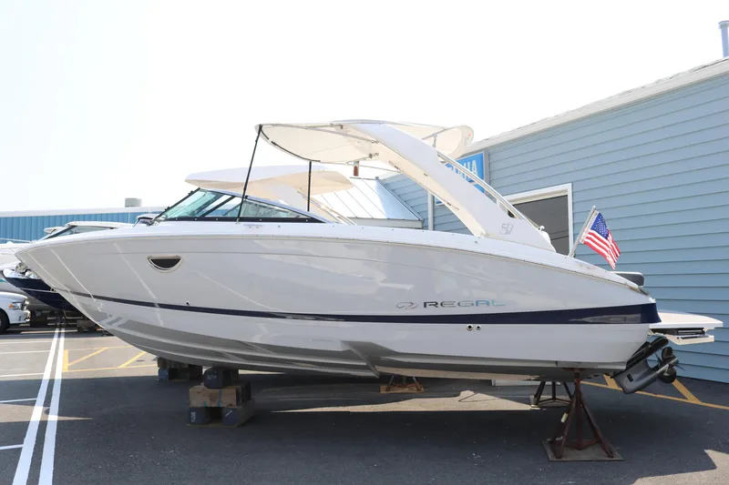 Slide: The Image of 2023 Regal LS6 boat on display, white exterior, American flag, parked on stands. - 2
