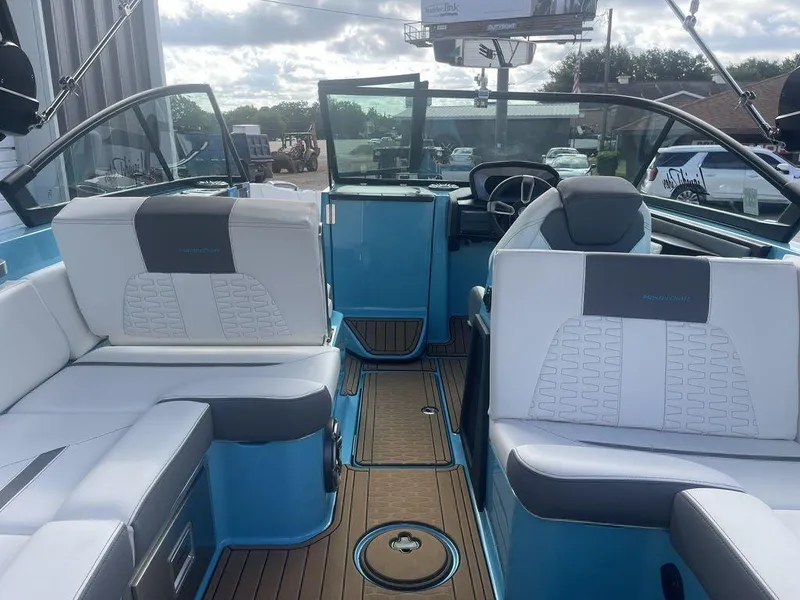 Slide: The Image of 2022 MasterCraft X26 boat interior with white and blue seating, modern dashboard, and wooden flooring. - 15