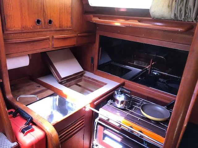Slide: The Image of Interior of 1981 Nautor Swan 371 Sloop, featuring a compact wooden kitchen with stove and storage. - 5