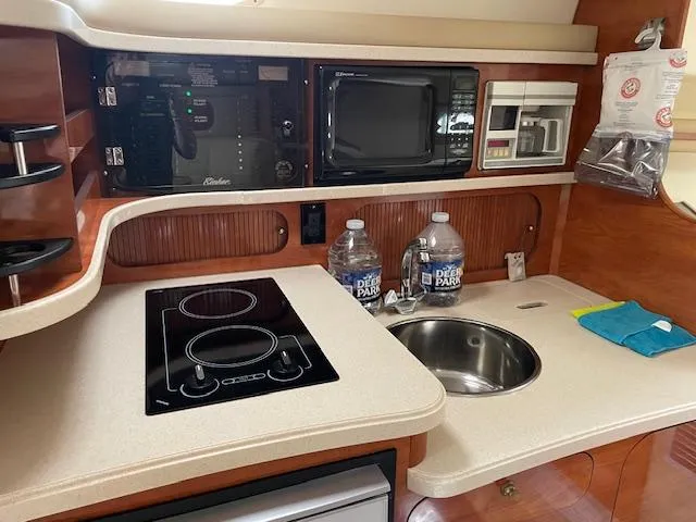 Slide: The Image of 2004 Rinker 342 Express Cruiser kitchen with stove, microwave, sink, and storage shelves. - 48