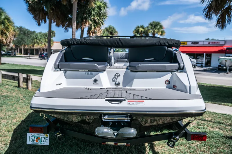 Slide: The Image of 2021 Scarab 195 boat rear view, parked on grass with palm trees and buildings in the background. - 4