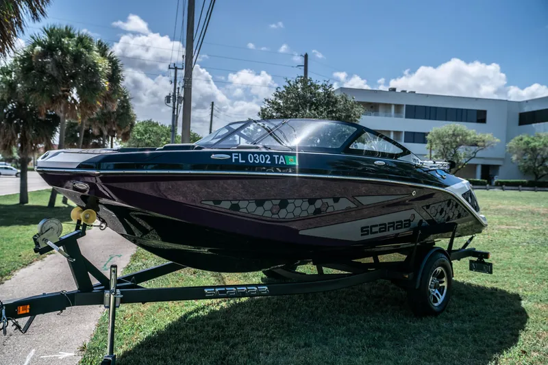 Slide: The Image of 2021 Scarab 195 boat on a trailer, parked outdoors near palm trees and buildings. - 7