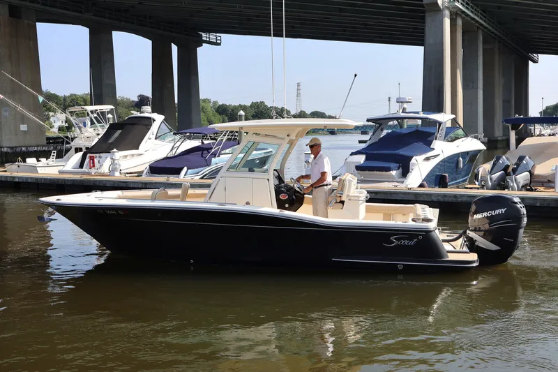 Slide: The Image of 2016 Scout 255 LXF boat docked under a bridge, with a person at the helm. - 1