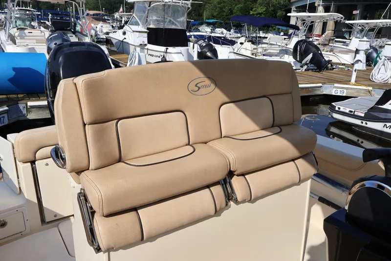 Slide: The Image of 2016 Scout 255 LXF boat seating at marina, featuring beige cushioned seats. - 12