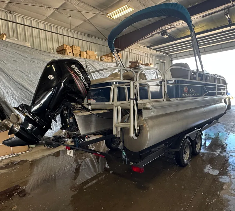 Slide: The Image of 2019 Sun Tracker SportFish 22 DLX pontoon boat in a garage with Mercury outboard motor. - 2