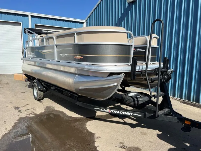 Slide: The Image of 2023 Sun Tracker PARTY BARGE® 18 DLX pontoon boat on trailer outside blue building. - 3