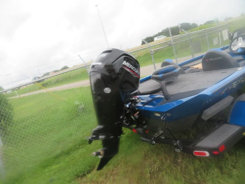 Slide: The Image of 2023 Vexus AVX 181 boat with Mercury outboard motor, parked on grass near a fence. - 19
