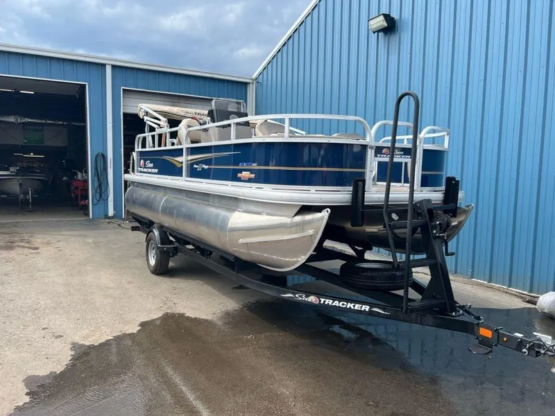 Slide: The Image of 2023 Sun Tracker BASS BUGGY® 18 DLX pontoon boat on trailer outside blue building. - 15