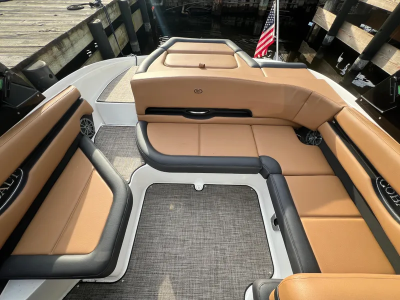 Slide: The Image of 2023 Cobalt CS23 Surf boat interior with tan and black seating, docked by wooden pier. - 12