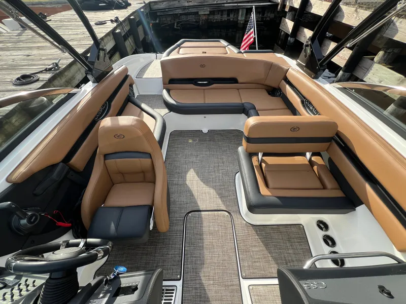 Slide: The Image of 2023 Cobalt CS23 Surf boat interior with tan and black seating, docked by wooden pier. - 18