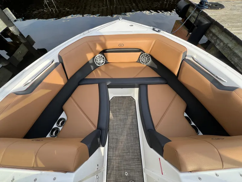Slide: The Image of 2023 Cobalt CS23 Surf boat interior with tan and black seating, docked by water. - 19