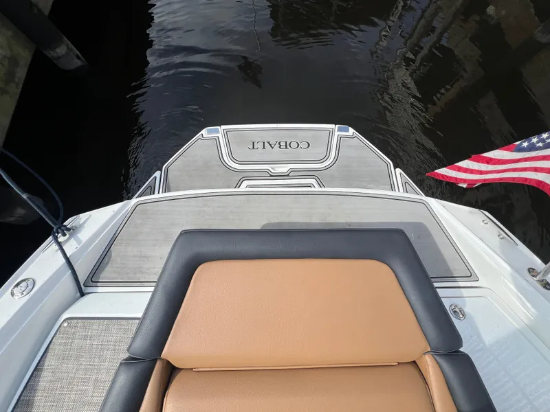 Slide: The Image of 2023 Cobalt CS23 Surf boat stern with American flag and cushioned seating. - 8