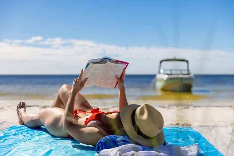 Slide: The Image of Woman reading on beach with 2023 Bayliner DX2000 boat in background. - 45