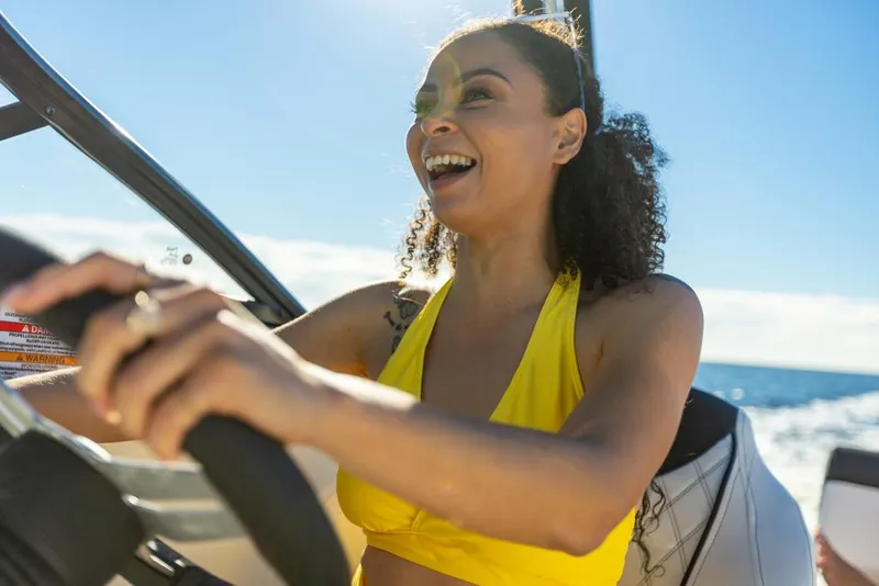 Slide: The Image of Woman driving 2023 Bayliner DX2050 boat, smiling under sunny sky. - 41