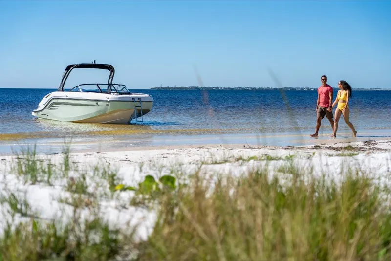 Slide: The Image of 2023 Bayliner DX2250 boat on a sandy beach with a couple walking nearby. - 26