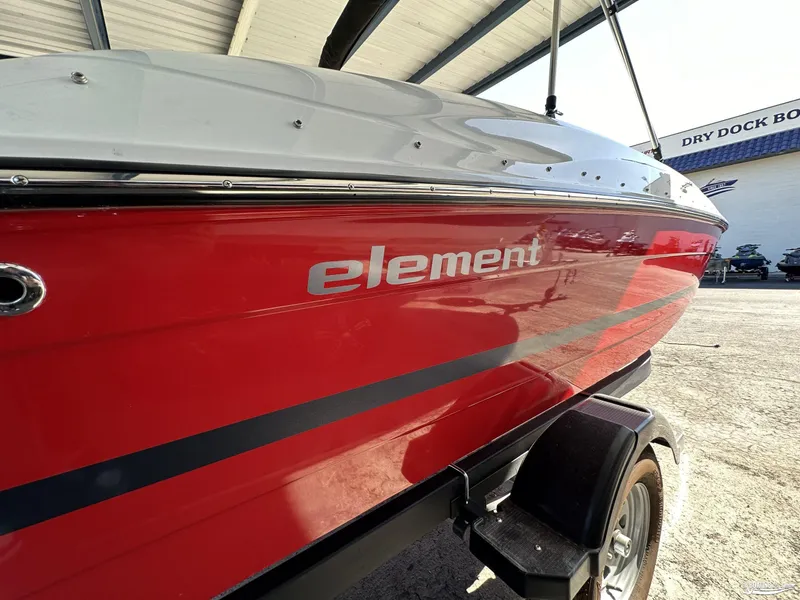 Slide: The Image of 2023 Bayliner E18 boat with red hull, parked in dry dock. - 2