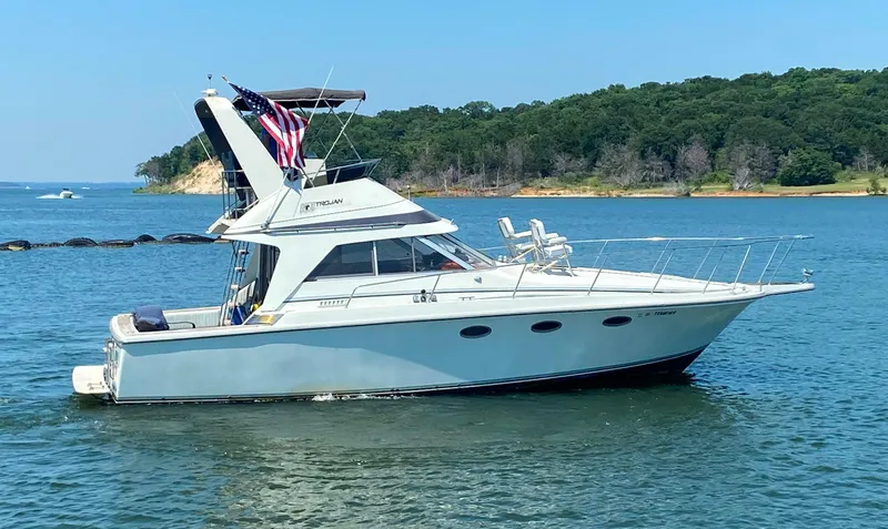 Slide: The Image of 1984 Trojan 10 Meter Sedan boat on a serene lake with lush green shoreline. - 6