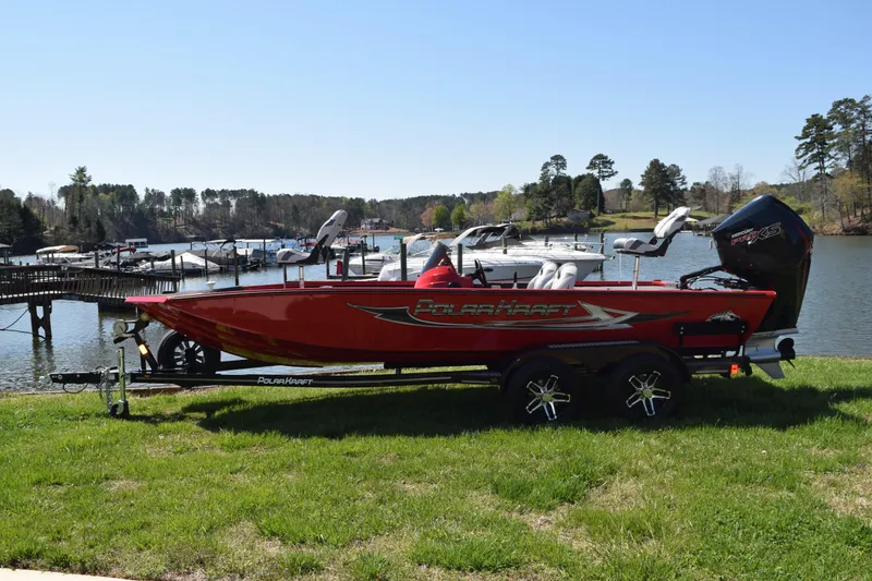 The Image of 2022 Polar Kraft Bass TX 195 Pro boat on trailer by a scenic lake. - 0