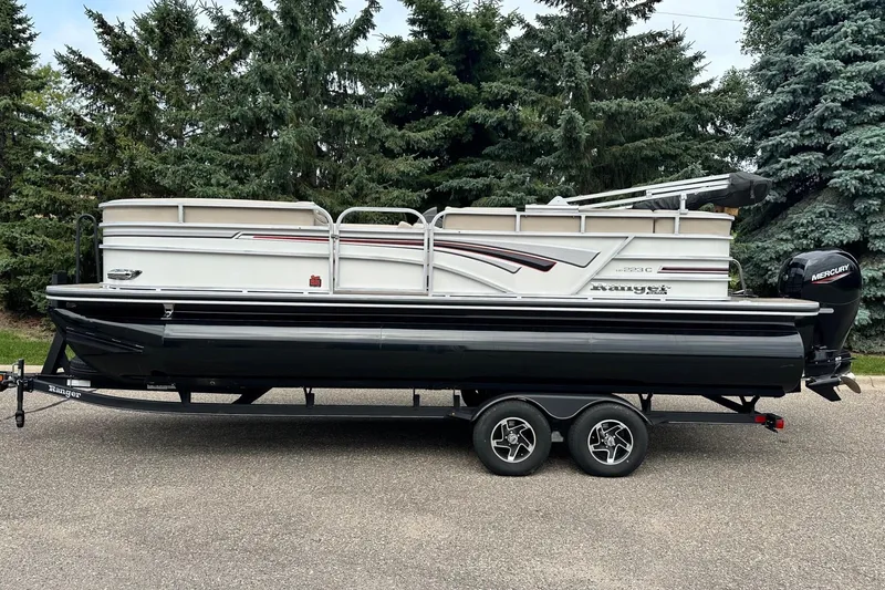 Slide: The Image of 2023 Ranger Reata 223C pontoon boat on trailer, parked near lush green trees. - 15